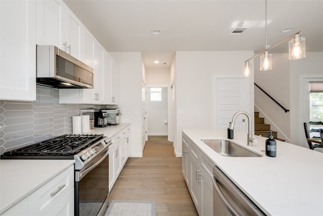 kitchen with appliances with stainless steel finishes, sink, light wood-type flooring, decorative light fixtures, and white cabinets