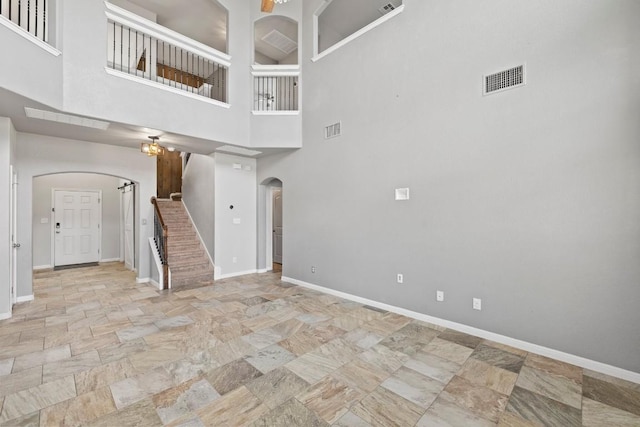 unfurnished living room with baseboards, stone finish flooring, visible vents, arched walkways, and stairway