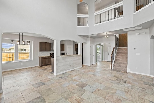 unfurnished living room featuring baseboards, arched walkways, and stone tile floors