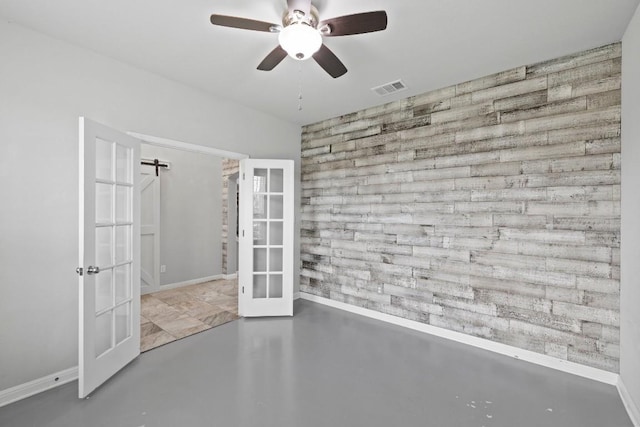 424 Hendelson Ln, Hutto, TX 78634 - unfurnished bedroom with french doors, an accent wall, baseboards, concrete floors, and a ceiling fan