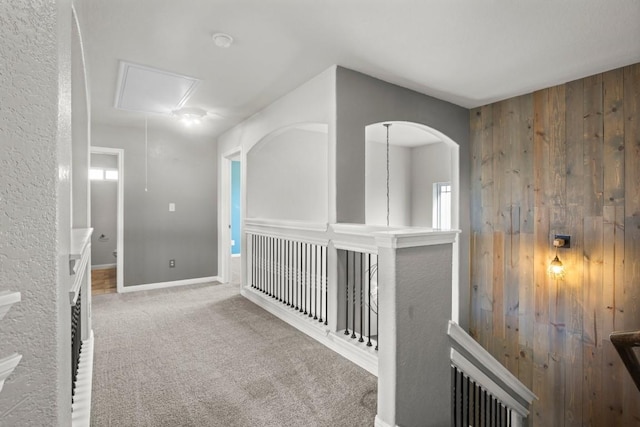 hallway with a healthy amount of sunlight, wooden walls, attic access, and carpet