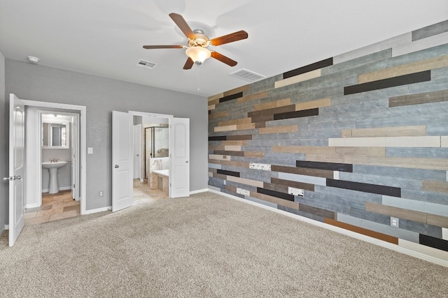 unfurnished bedroom featuring wooden walls, ceiling fan, ensuite bath, light colored carpet, and sink