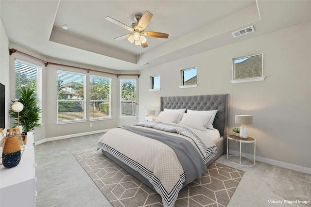 carpeted bedroom featuring multiple windows, a tray ceiling, and ceiling fan