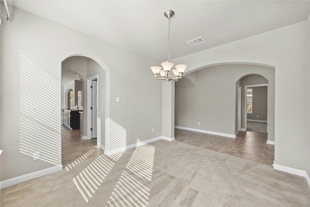 spare room featuring a wealth of natural light, a chandelier, and light colored carpet