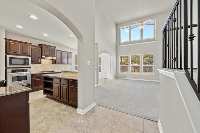 kitchen with light stone countertops, a towering ceiling, ceiling fan, stainless steel appliances, and dark brown cabinetry