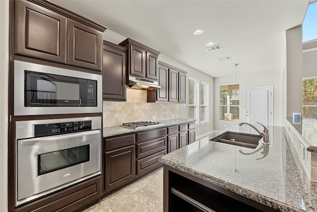 kitchen featuring stainless steel appliances, sink, dark brown cabinetry, light stone counters, and tasteful backsplash