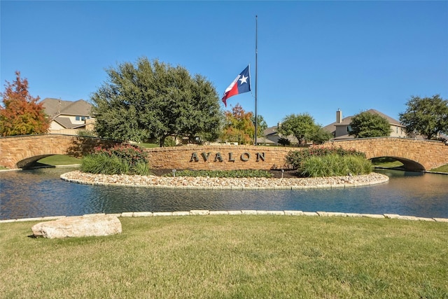 community / neighborhood sign featuring a water view and a lawn