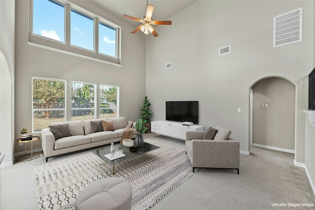 carpeted living room with a high ceiling, ceiling fan, and plenty of natural light