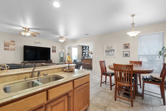 kitchen with sink, light tile patterned flooring, light stone counters, and decorative light fixtures