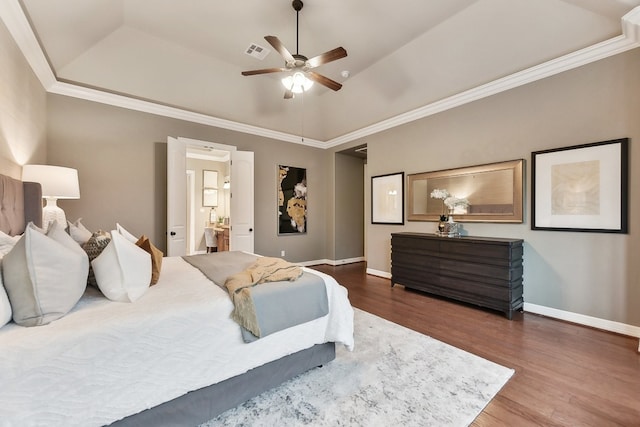 bedroom featuring hardwood / wood-style flooring, ensuite bath, crown molding, a raised ceiling, and ceiling fan