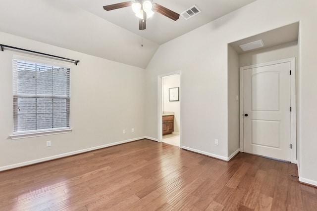 unfurnished bedroom with lofted ceiling, wood-type flooring, connected bathroom, and ceiling fan