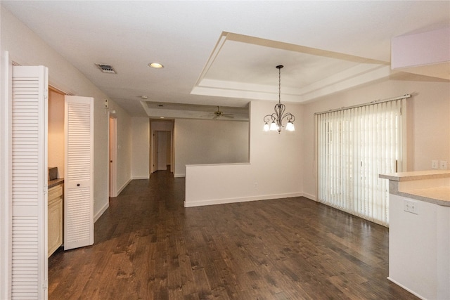 unfurnished dining area featuring ceiling fan with notable chandelier, a raised ceiling, and dark hardwood / wood-style flooring