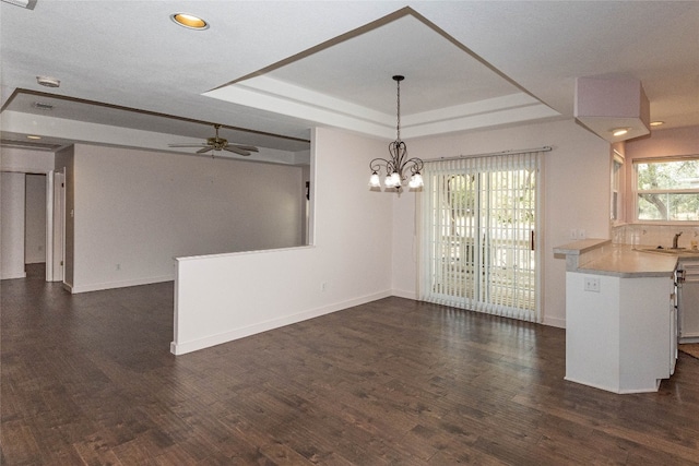 interior space featuring dark wood-type flooring, ceiling fan with notable chandelier, sink, and a tray ceiling