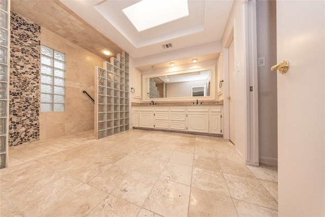 bathroom featuring vanity, a tile shower, a skylight, and a tray ceiling