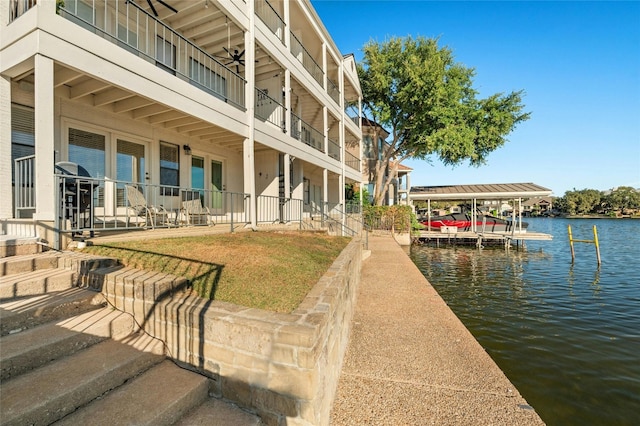 dock area featuring a balcony, a water view, and a lawn