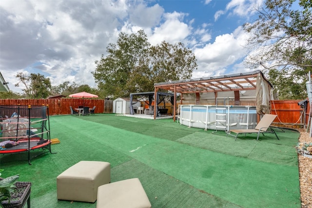 view of yard featuring a storage unit, a trampoline, and a fenced in pool