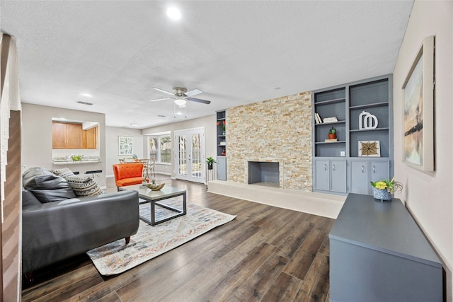 living room featuring a stone fireplace, ceiling fan, built in features, and a textured ceiling