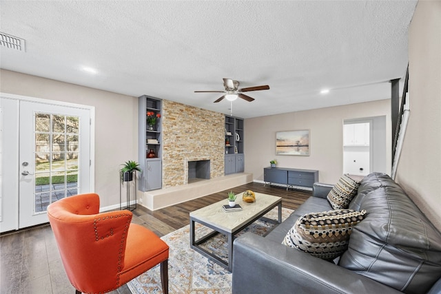 living room featuring built in shelves, a stone fireplace, and a textured ceiling