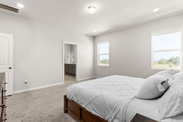 carpeted bedroom with ensuite bath and multiple windows