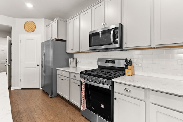 kitchen with white cabinets, light stone countertops, tasteful backsplash, dark hardwood / wood-style flooring, and stainless steel appliances