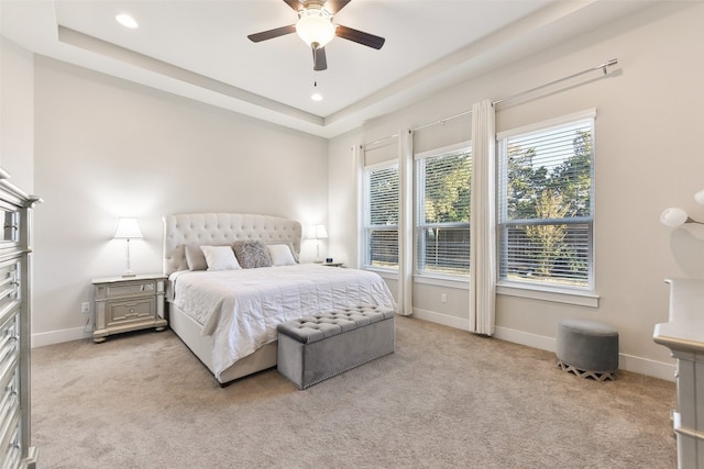 bedroom featuring light colored carpet, a tray ceiling, and ceiling fan