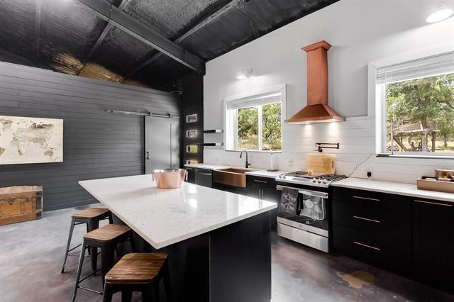 kitchen with a center island, stainless steel gas range oven, wall chimney range hood, sink, and a kitchen bar