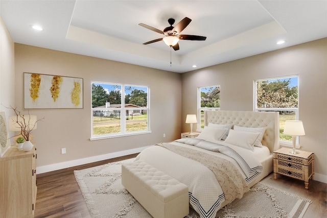 bedroom with dark wood-type flooring, a raised ceiling, and ceiling fan