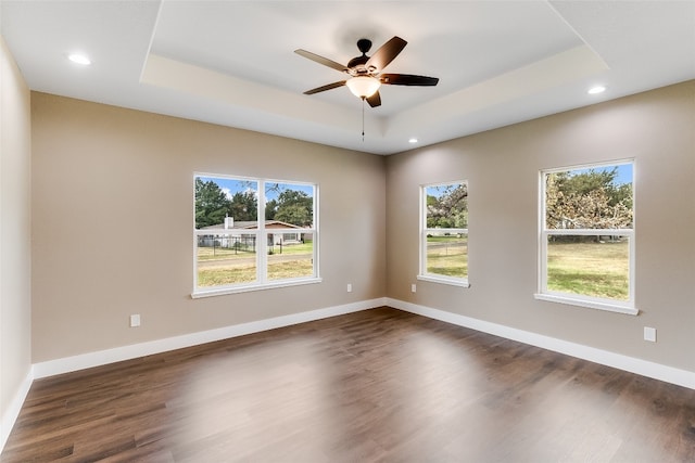 spare room featuring ceiling fan, dark wood-type flooring, a raised ceiling, and a wealth of natural light