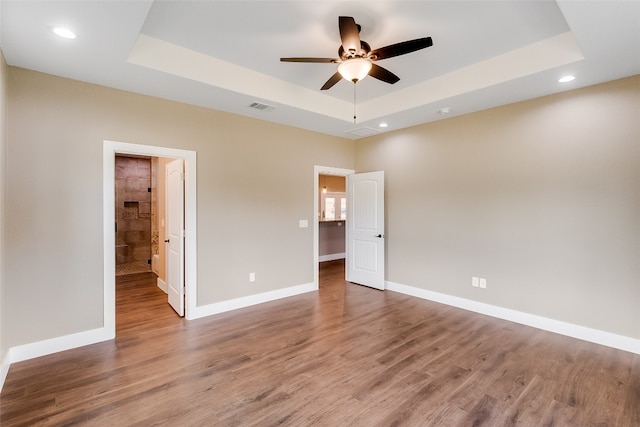 unfurnished bedroom with ceiling fan, a raised ceiling, ensuite bathroom, and hardwood / wood-style floors