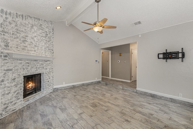 unfurnished living room with ceiling fan, a textured ceiling, a fireplace, light hardwood / wood-style floors, and lofted ceiling with beams