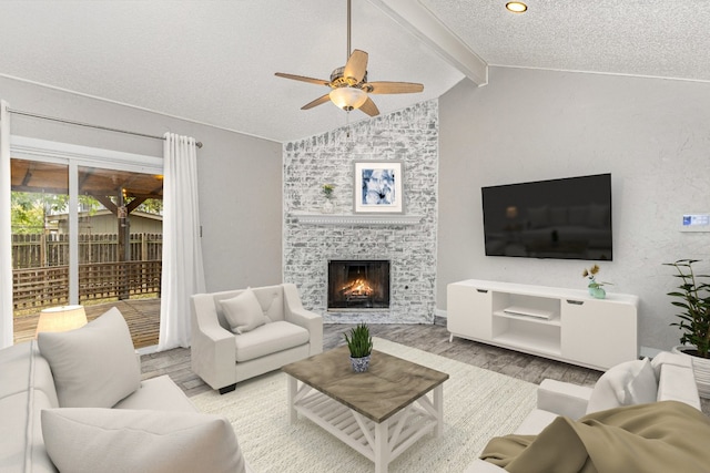 living room with a fireplace, lofted ceiling with beams, a textured ceiling, light hardwood / wood-style floors, and ceiling fan