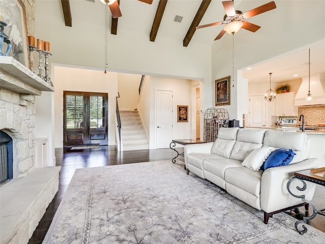 living room featuring a fireplace, ceiling fan with notable chandelier, hardwood / wood-style floors, beam ceiling, and high vaulted ceiling