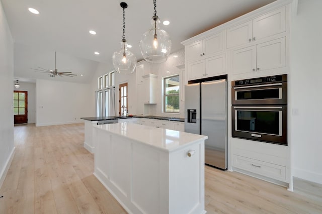 kitchen with stainless steel appliances, a center island, pendant lighting, light wood-type flooring, and white cabinetry