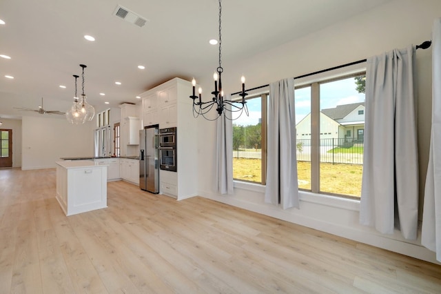 kitchen featuring appliances with stainless steel finishes, a kitchen island, white cabinetry, decorative light fixtures, and light hardwood / wood-style flooring