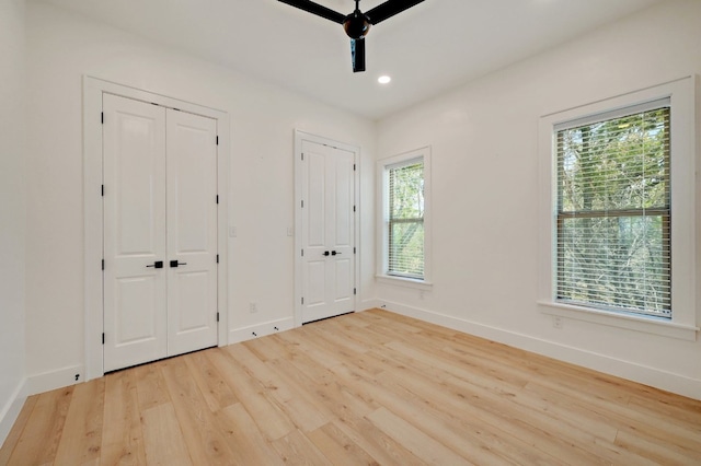 unfurnished bedroom with two closets, multiple windows, light wood-type flooring, and ceiling fan