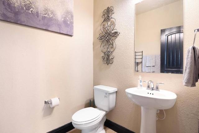 half bathroom with toilet, baseboards, and a textured wall