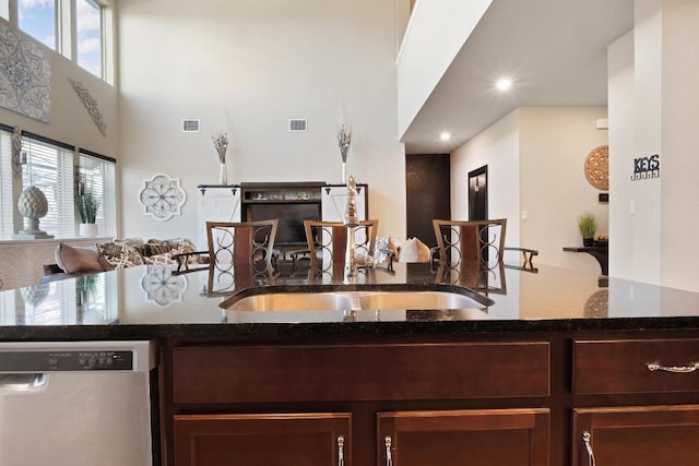 kitchen featuring sink, dark brown cabinetry, dark stone counters, and stainless steel dishwasher