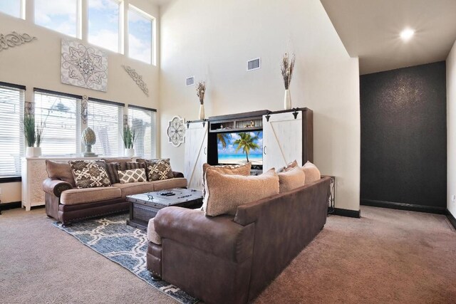 living room with a barn door, carpet flooring, and a towering ceiling