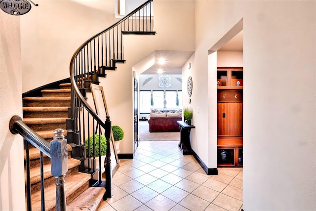 entryway featuring a towering ceiling, light tile patterned floors, stairway, and baseboards