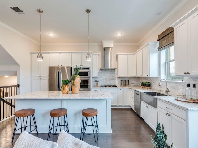 kitchen featuring hanging light fixtures, wall chimney exhaust hood, a kitchen island, white cabinetry, and stainless steel appliances