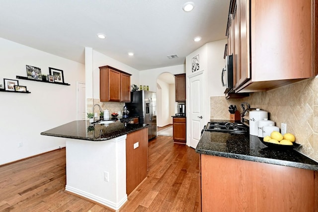 kitchen featuring sink, stainless steel fridge with ice dispenser, kitchen peninsula, dark stone counters, and light wood-type flooring