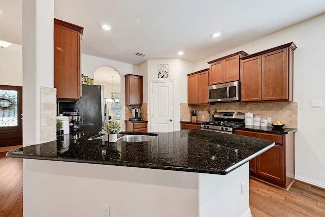 kitchen with kitchen peninsula, light hardwood / wood-style flooring, appliances with stainless steel finishes, and dark stone counters