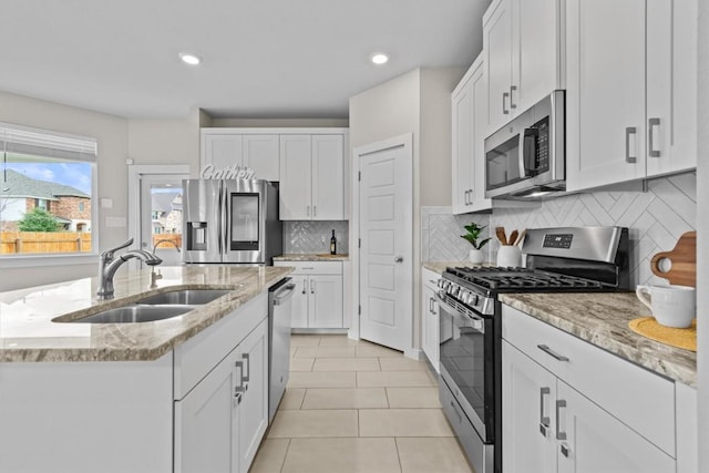 kitchen featuring sink, light stone counters, decorative backsplash, white cabinets, and appliances with stainless steel finishes