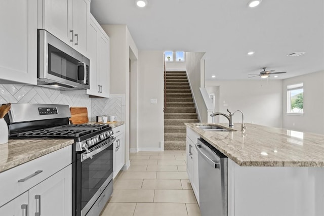 kitchen featuring white cabinetry, sink, light stone countertops, a center island with sink, and appliances with stainless steel finishes