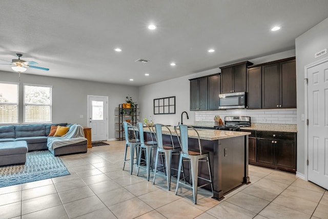 kitchen with an island with sink, a breakfast bar area, appliances with stainless steel finishes, backsplash, and light stone counters