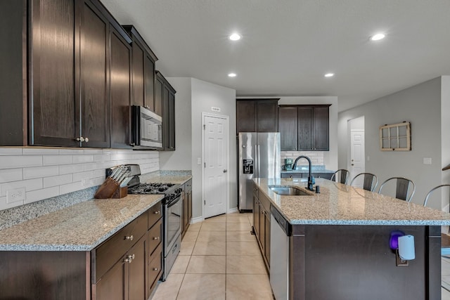 kitchen with light stone countertops, stainless steel appliances, sink, backsplash, and a kitchen island with sink