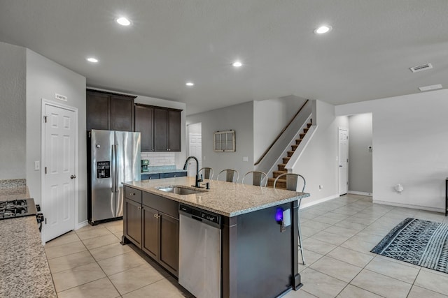 kitchen with stainless steel appliances, a kitchen island with sink, a kitchen breakfast bar, dark brown cabinets, and sink