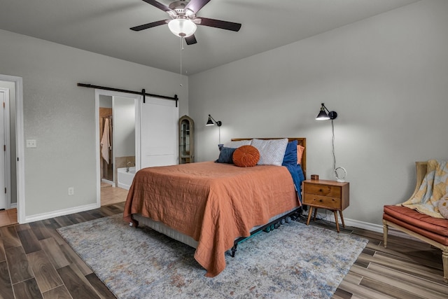 bedroom featuring ceiling fan, ensuite bathroom, dark hardwood / wood-style flooring, and a barn door