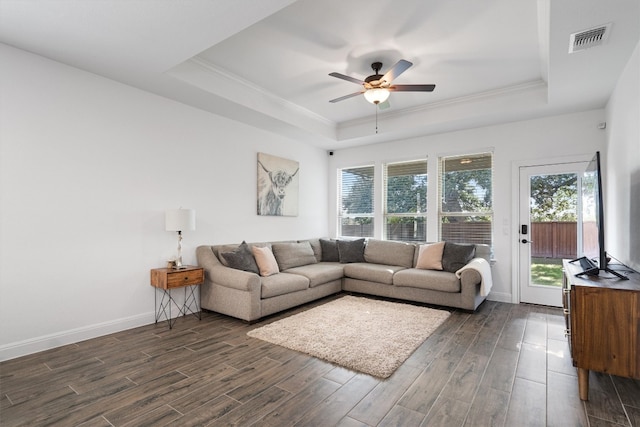 living room with dark wood-type flooring, crown molding, a tray ceiling, and ceiling fan