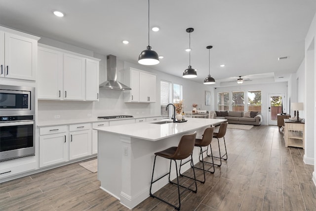 kitchen featuring a wealth of natural light, appliances with stainless steel finishes, wall chimney range hood, and white cabinetry